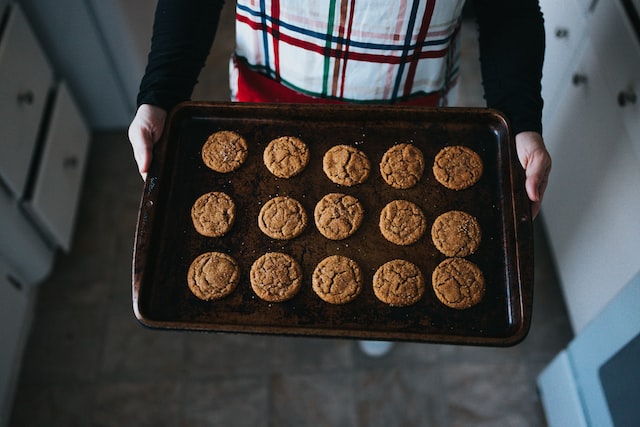 A person holds a black baking pan filled with ginger snap cookies.