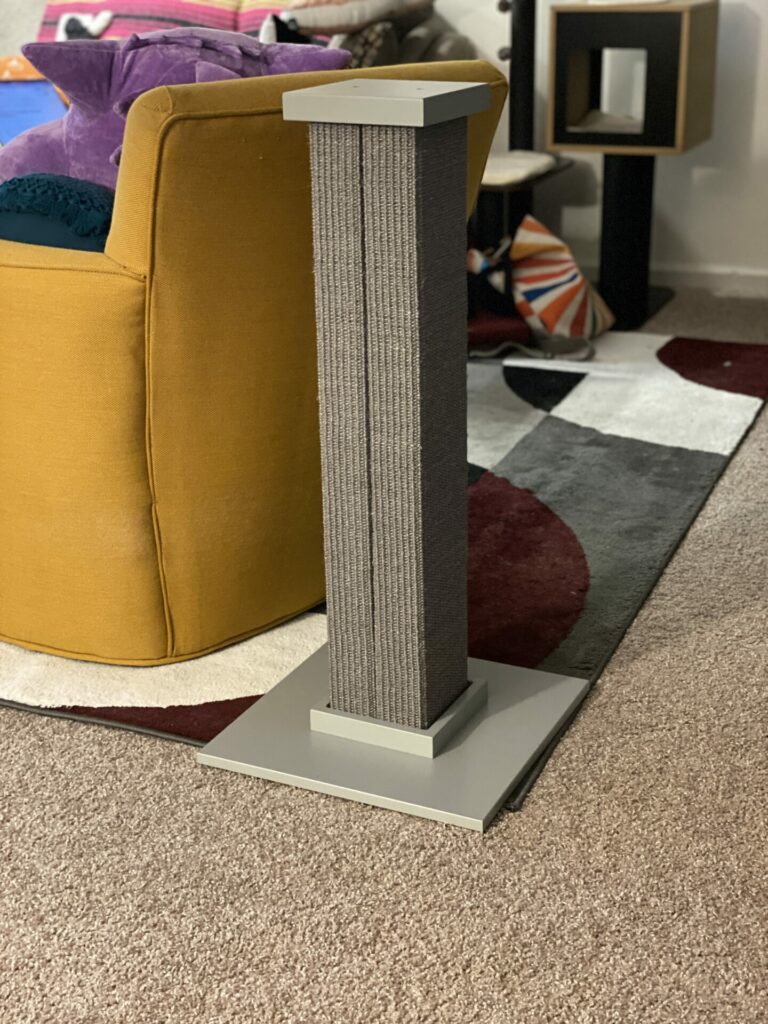 The SmartCat Ultimate Scratching Post in gray in Joey's living room near a yellow chair that was being scratched by his cat.