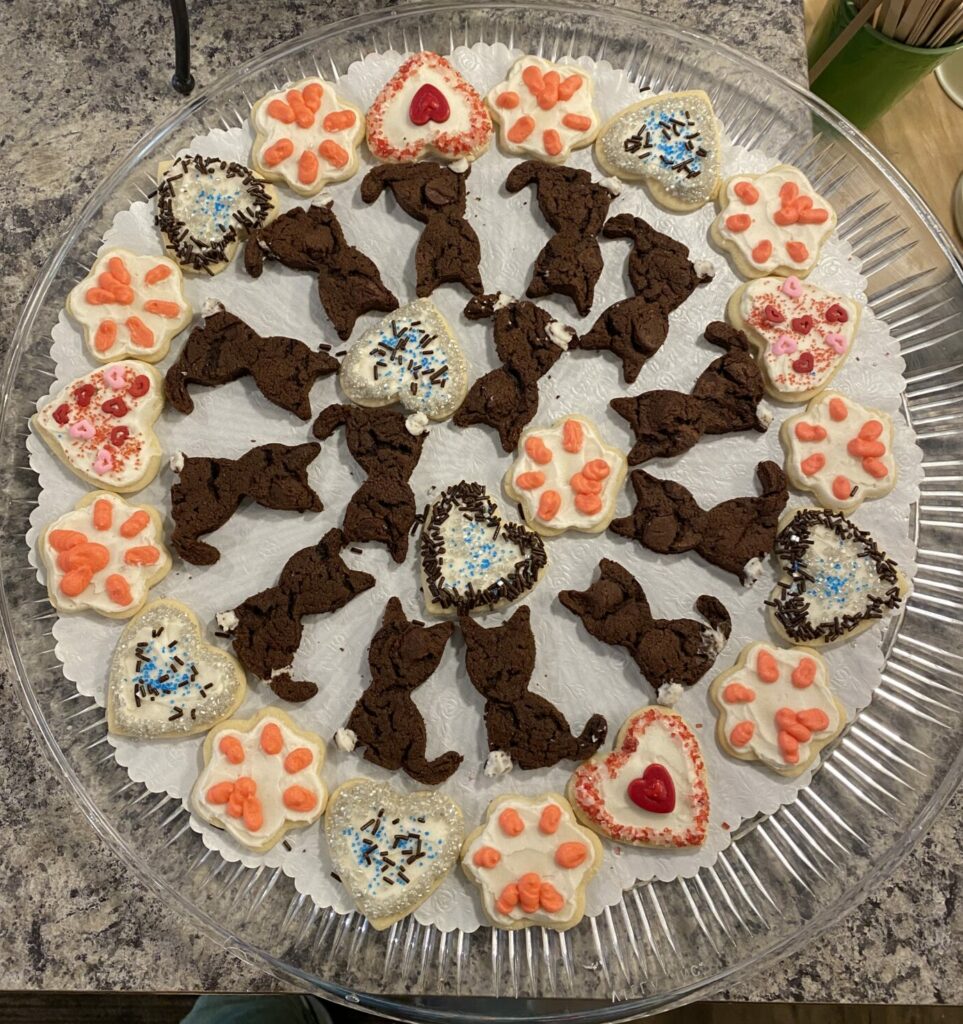 A tray of cookies in the shape of cats, paw prints, hearts with blue, silver, and brown sprinkles.