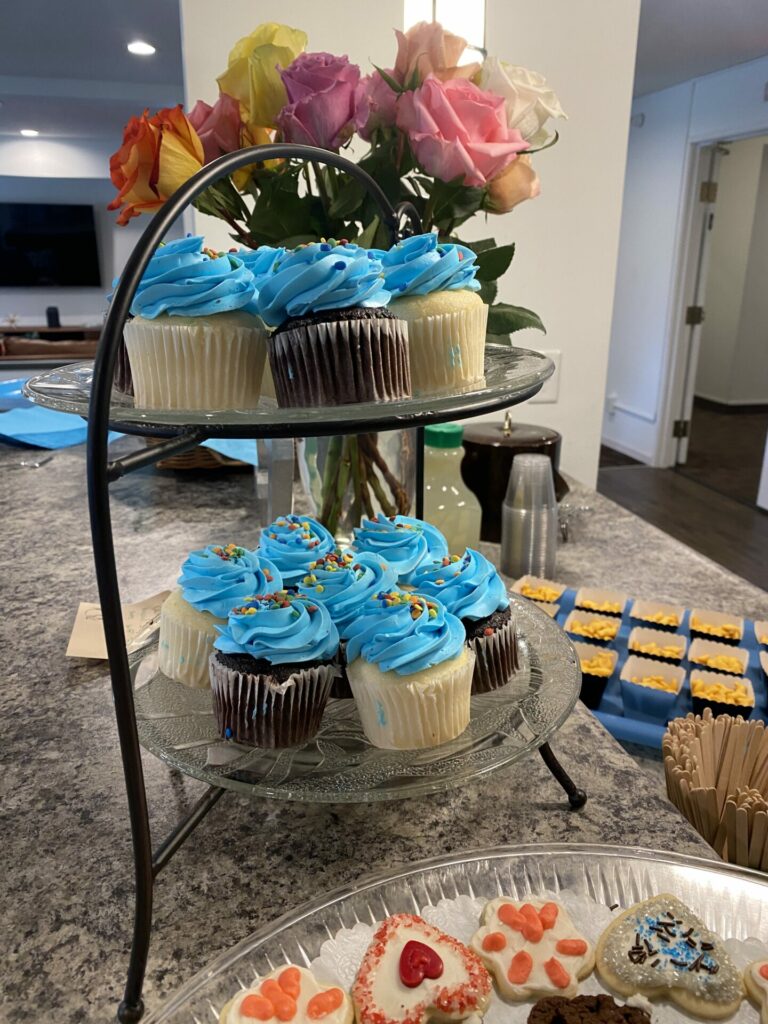 A tray with blue frosted cupcakes and roses in the background.