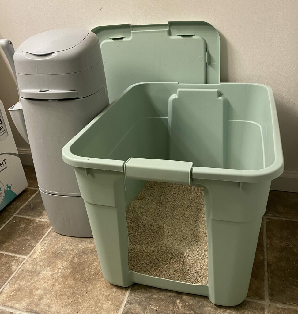 A mint green storage tub turned into a DIY litter box with a large entry cut into the front. A gray Litter Genie sits to the left.